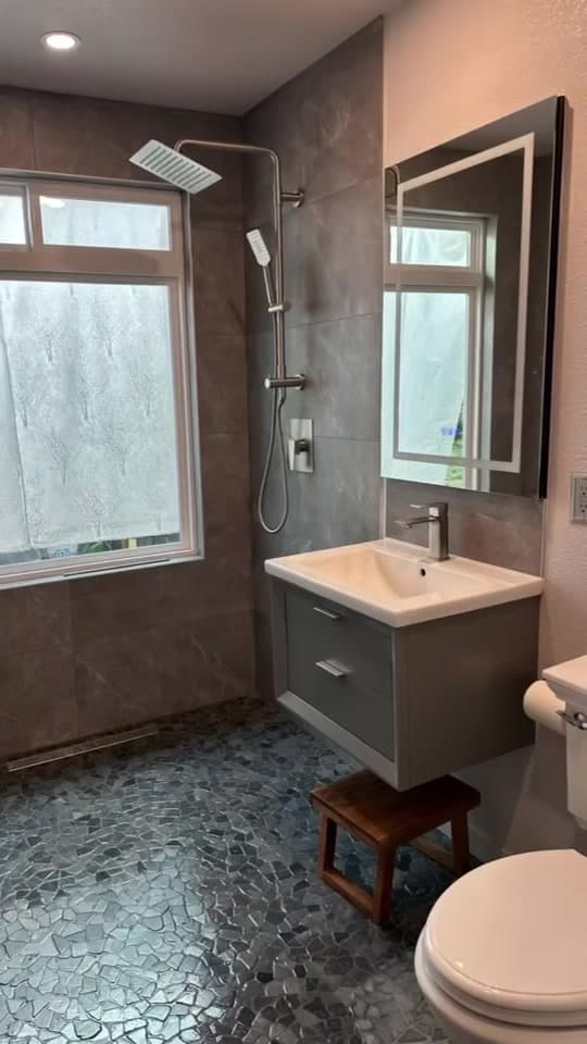Finished bathroom with grey tile walls, a walk-in shower, a floating vanity, and a pebble-mosaic floor.